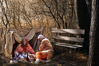 Homeless elderly couple sitting by makeshift shelter in woods
