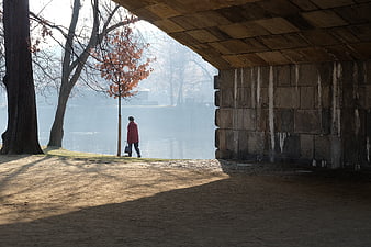 Woman in Red Coat Walking Under Stone Bridge by Lake