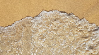 Aerial view of foamy ocean waves washing over golden sand