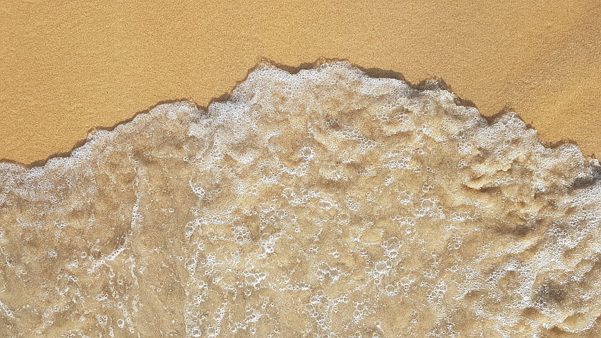 Aerial view of foamy ocean waves washing over golden sand