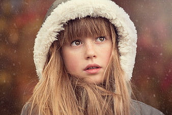 Close-up portrait of a girl in a hood looking up in snow