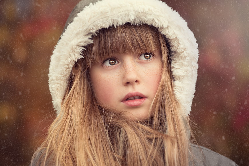 Close-up portrait of a girl in a hood looking up in snow