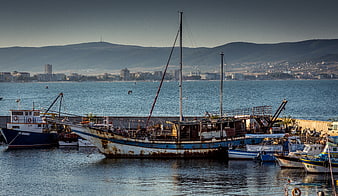 Rusty fishing boats docked in a harbor with city skyline