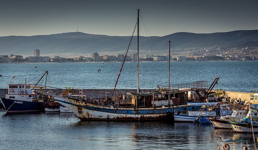 Rusty fishing boats docked in a harbor with city skyline