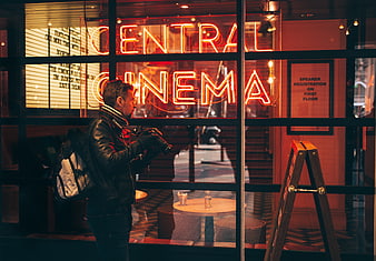 Photographer with camera outside Central Cinema neon sign