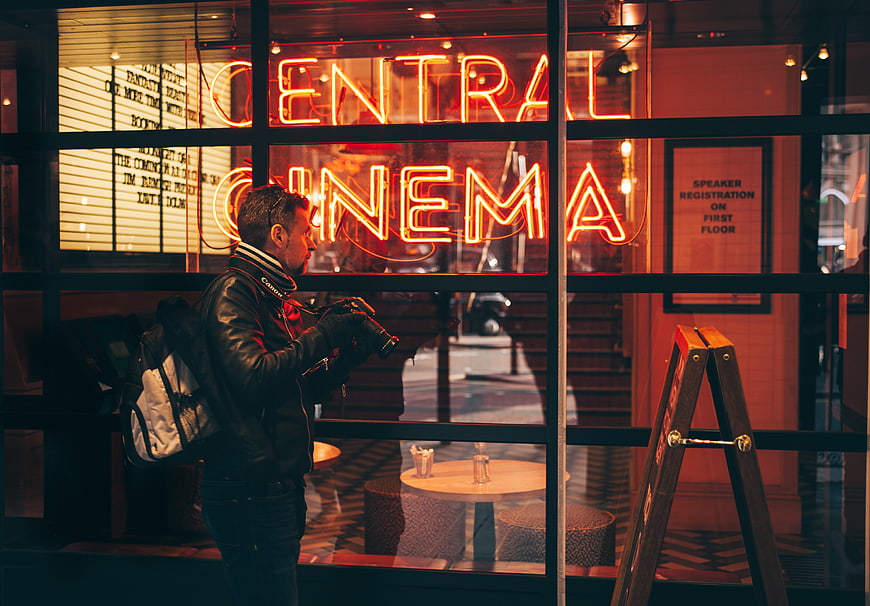 Photographer with camera outside Central Cinema neon sign