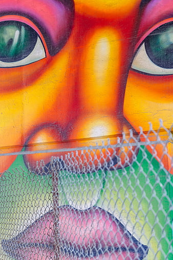 Vibrant graffiti mural face behind chain link fence