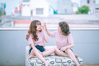 Two young women laughing and playing on a rooftop sofa