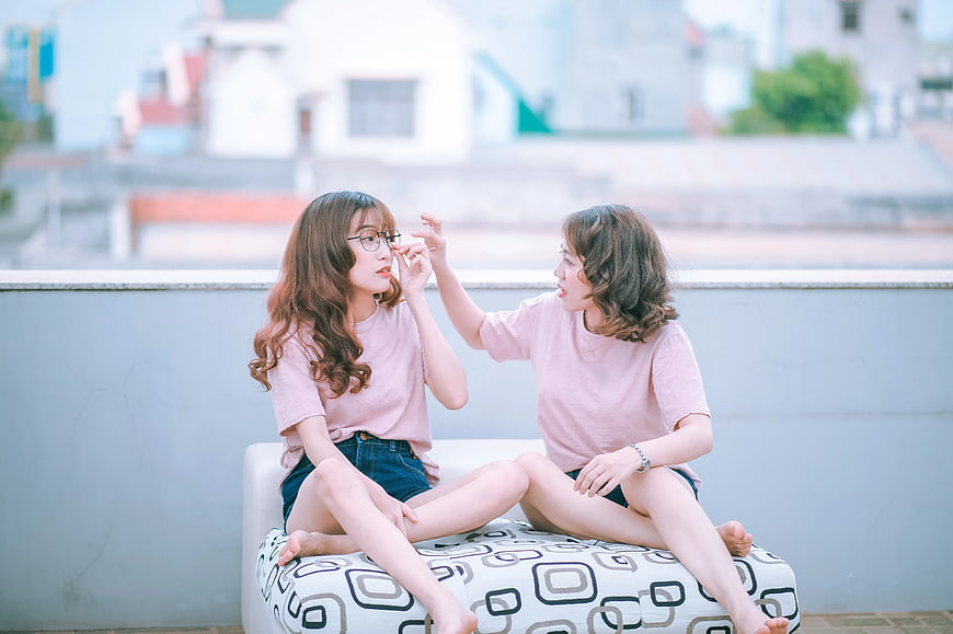 Two young women laughing and playing on a rooftop sofa