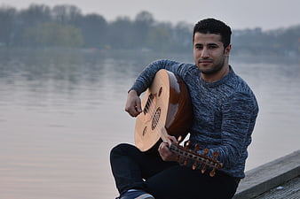 Man playing Oud by the lake at dusk