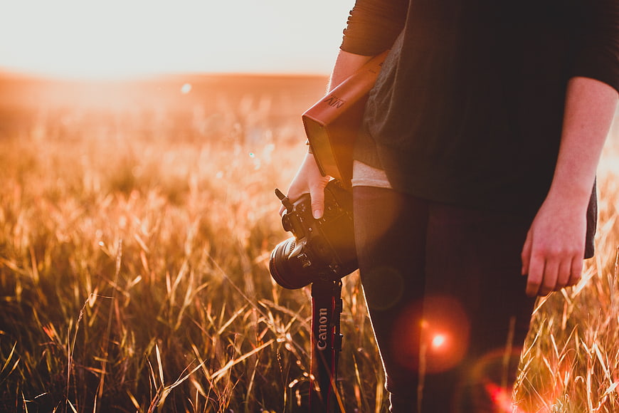 Photographer holding camera and Bible in golden wheat field at sunset