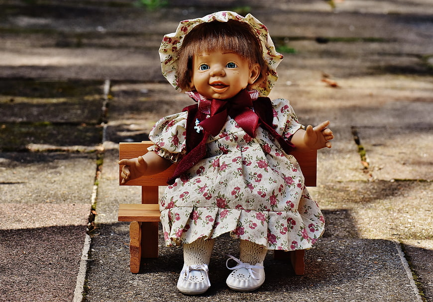 Vintage Doll in Floral Dress Sitting on Wooden Bench