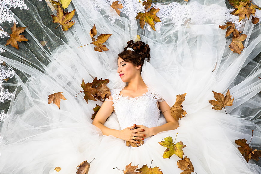 Bride in White Wedding Dress Lying on Autumn Leaves