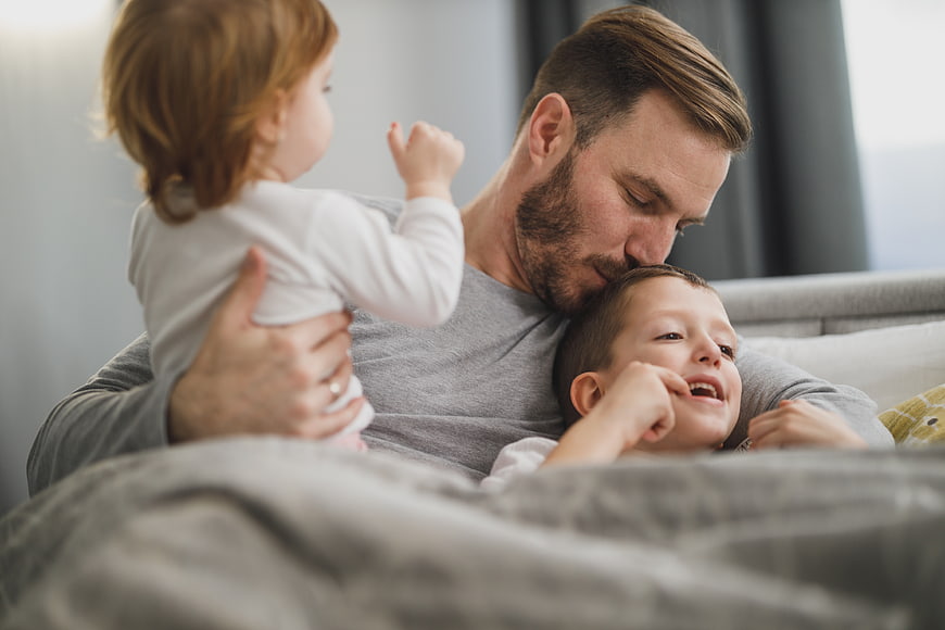 Father cuddling with two young children in bed