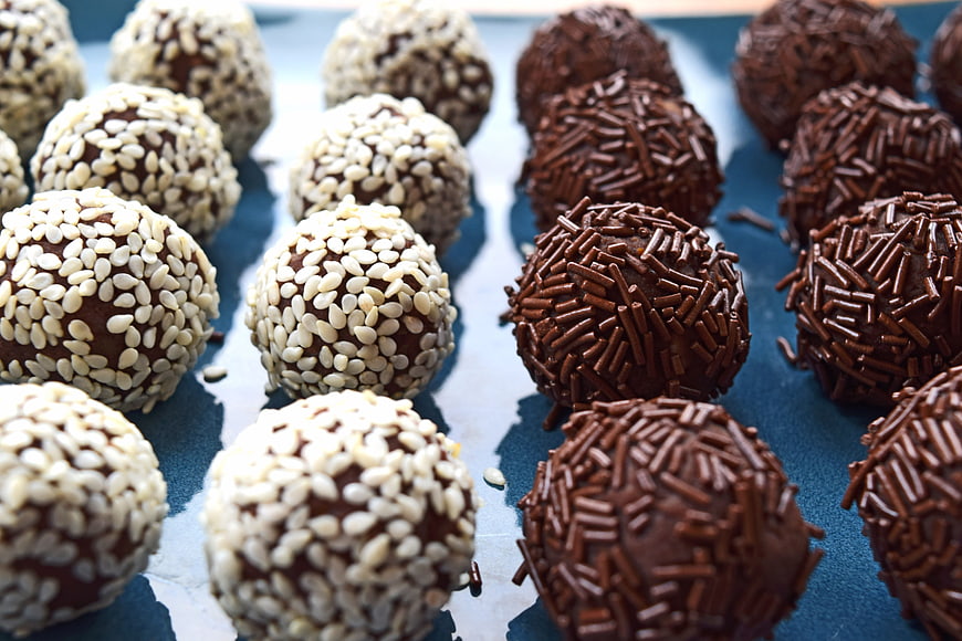 Chocolate truffles with sesame seeds and sprinkles on blue background