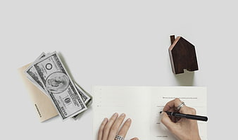 Hands writing in planner with cash and wooden house model on white desk