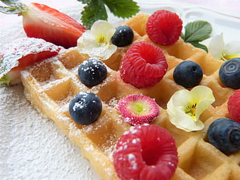 Golden waffle topped with fresh raspberries, blueberries, strawberries, and edible flowers