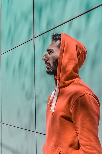 Man in Orange Hoodie Against Teal Wall