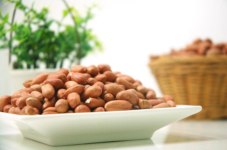 Raw Peanuts in Shells in White Bowl with Blurred Green Plant Background