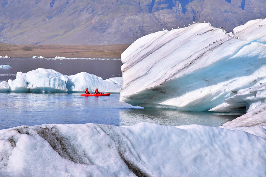 Kayakers paddling near massive blue icebergs in Iceland