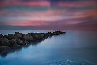 Long Exposure Pink Sunset Over Rocky Jetty and Calm Ocean