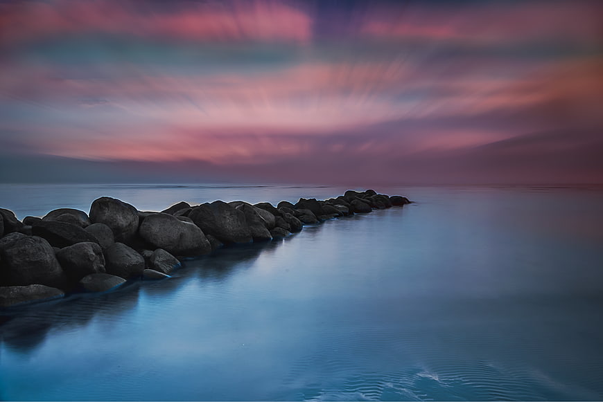 Long Exposure Pink Sunset Over Rocky Jetty and Calm Ocean