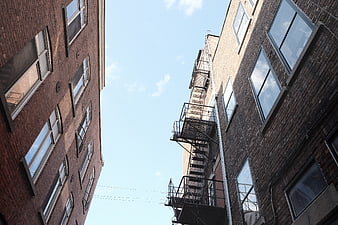 Low angle view of brick buildings with fire escape and blue sky