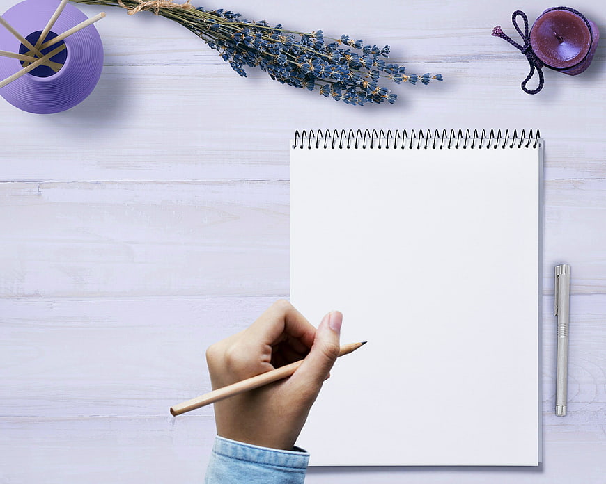 Hand holding pencil over blank notebook with lavender and candle