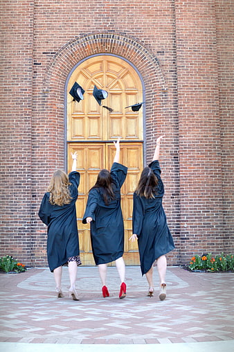 Three female graduates throwing caps in front of brick building