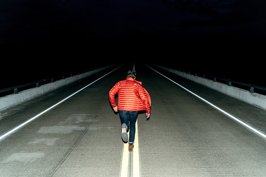 Man in Red Jacket Running on Dark Road at Night