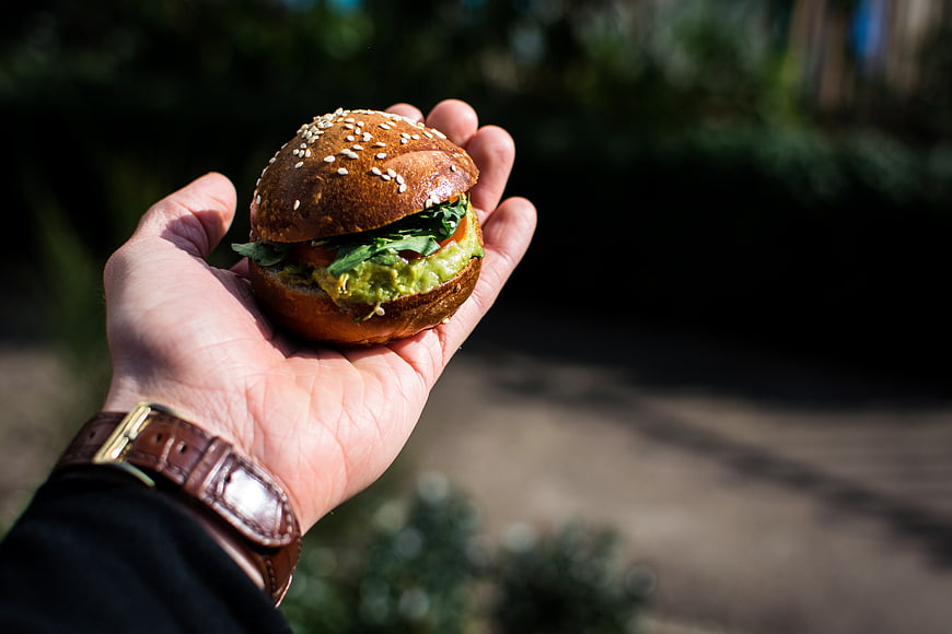 Hand holding mini burger with guacamole outdoors