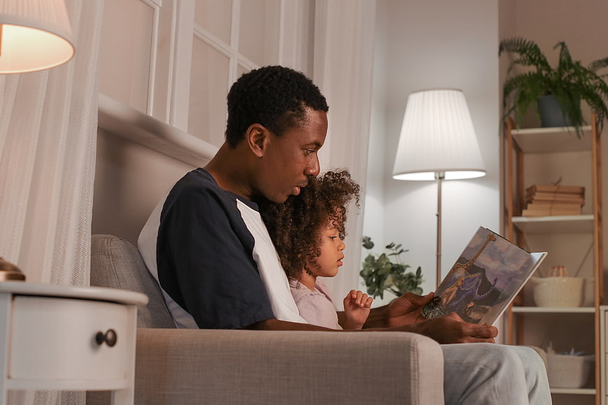 Father reading bedtime story to daughter on couch