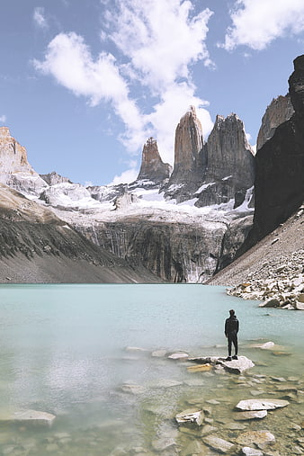 Hiker standing on rock in turquoise glacial lake with mountains