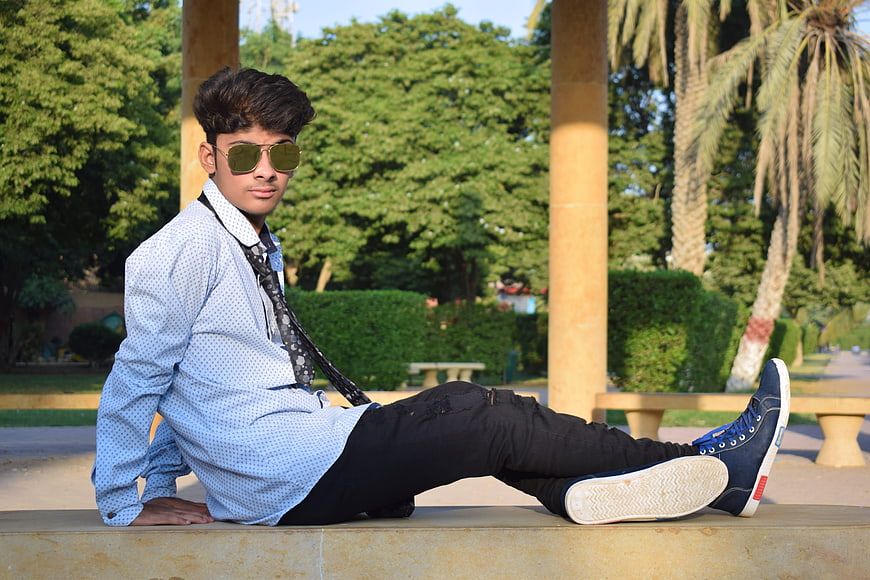 Stylish young man sitting on a park bench wearing sunglasses