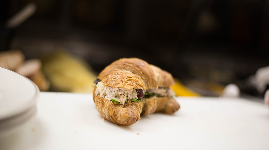 Close-up of a savory croissant sandwich on a white surface