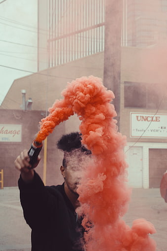 Man holding orange smoke grenade in urban alley