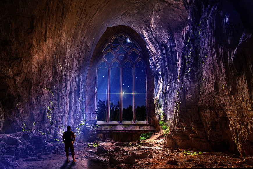 Man standing in cave looking at gothic window with starry night sky
