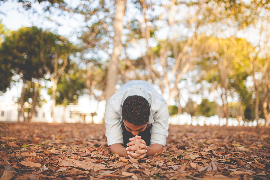 Man Praying on Ground Covered in Autumn Leaves