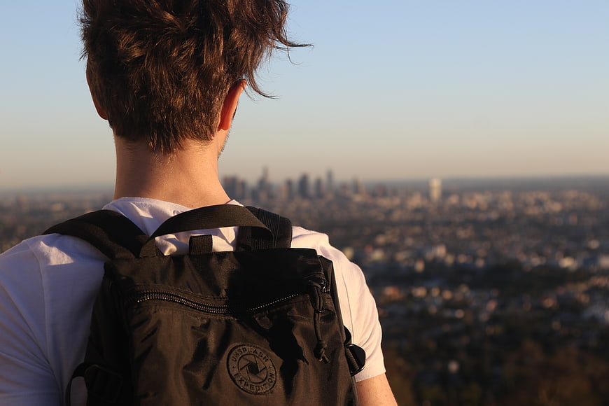 Man with Backpack Looking at City Skyline from Hilltop