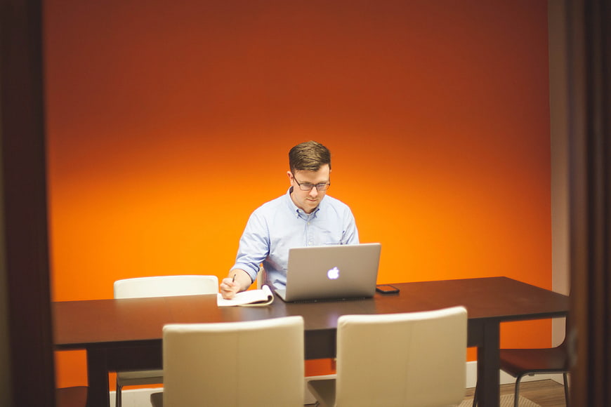 Man working on laptop in modern office with orange wall
