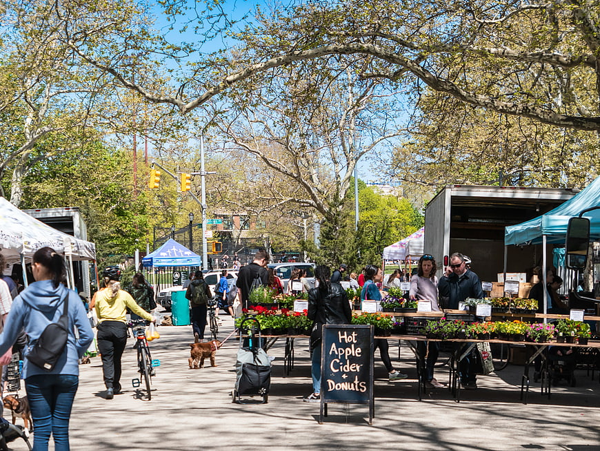 Busy outdoor farmers market with people, flowers, and food trucks