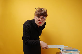Humorous female teacher making a funny face with a ruler and books