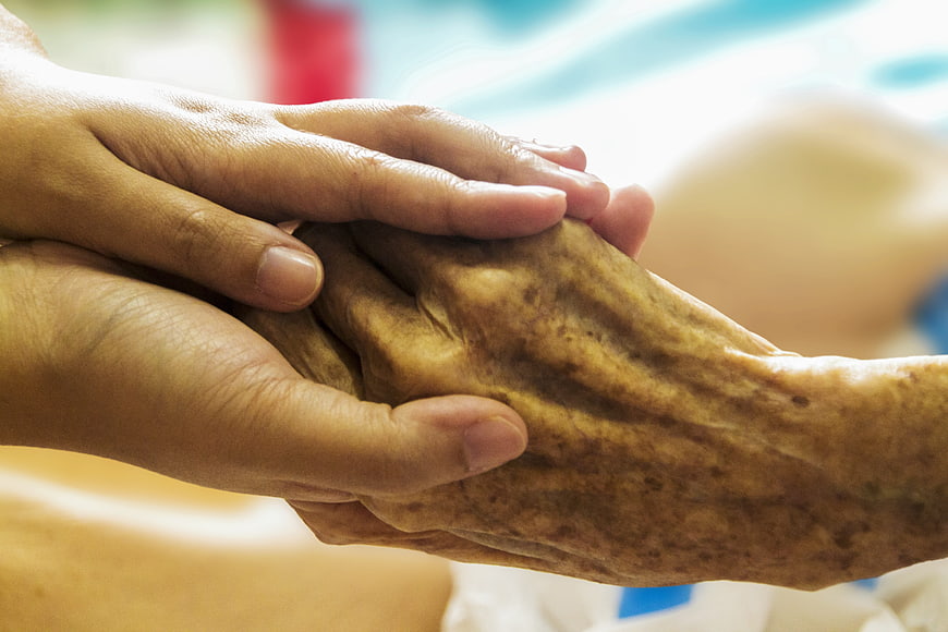 Close-up of young hands holding elderly hand in care