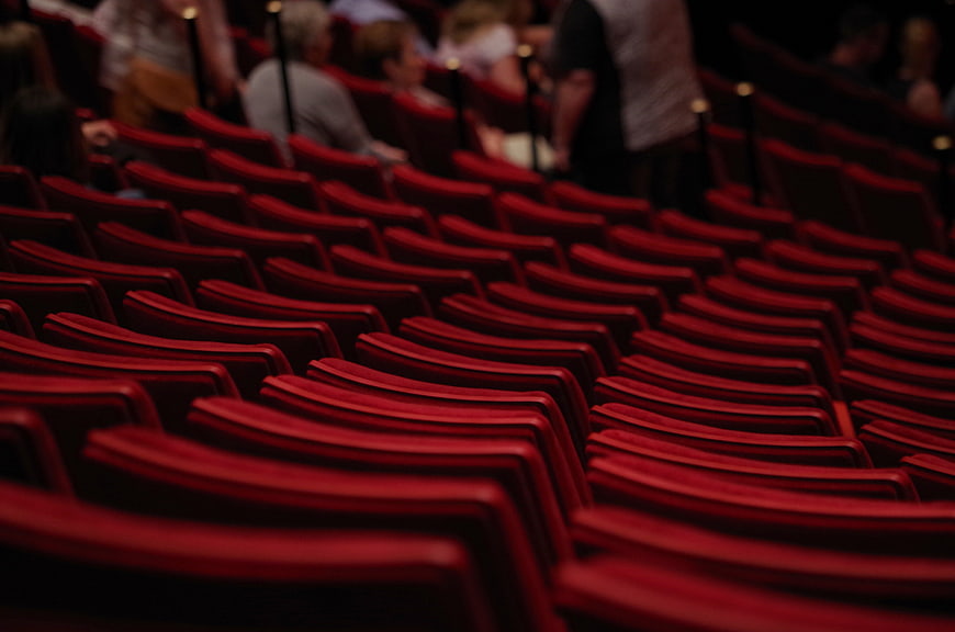 Rows of empty red theater seats with blurred audience