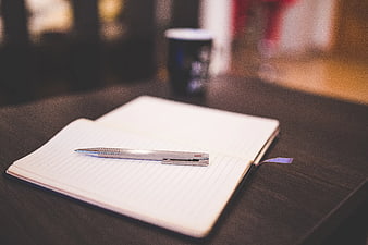 Silver pen on open notebook with coffee cup background