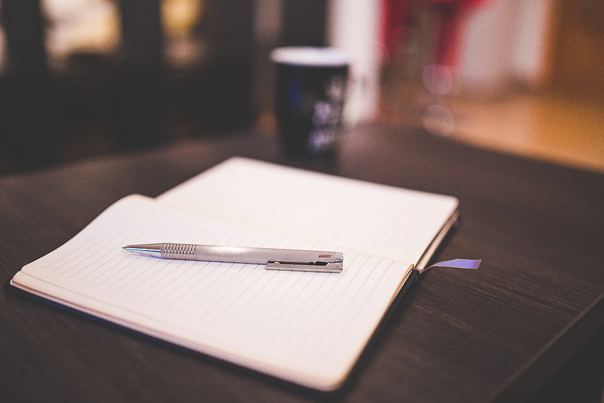 Silver pen on open notebook with coffee cup background