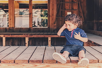 Cute curly-haired toddler boy sitting on wooden porch