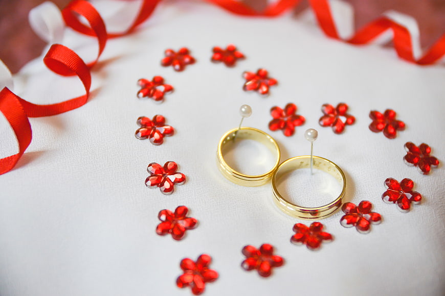 Gold wedding rings with red flower confetti on white background
