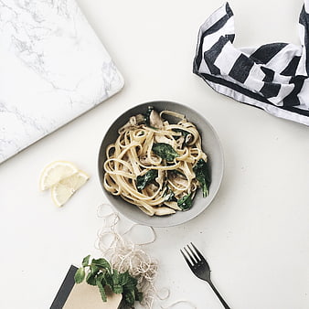 Flat lay of creamy pasta with spinach and mushrooms on white table