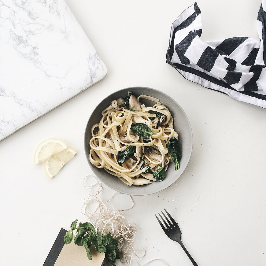 Flat lay of creamy pasta with spinach and mushrooms on white table